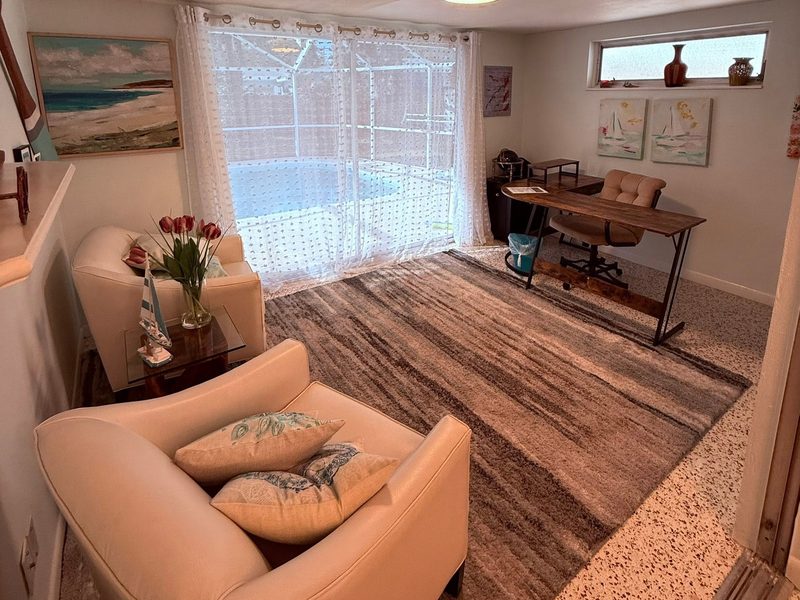Cleaned and staged rental living room with armchairs, an area rug and a screened pool beyond the sliding doors