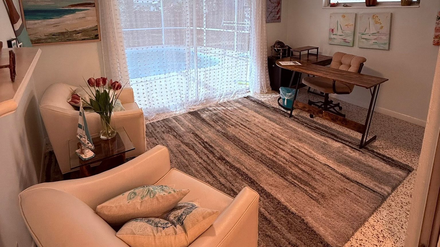 Cleaned and staged rental living room with armchairs, an area rug and a screened pool beyond the sliding doors